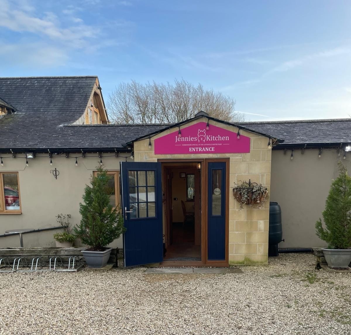Jennie's Kitchen entrance — a beautiful Cotswold stone building with pink signage in Ashton Keynes